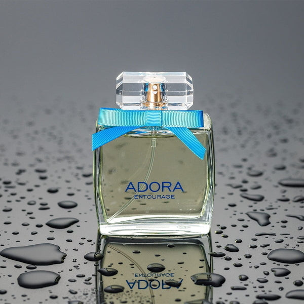 Sticlă pătrată de parfum „ADORA Entourage” cu capac transparent și fundă albastră, detalii aurii.