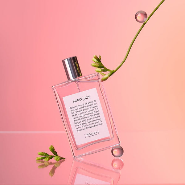 Sticlă elegantă apă de parfum #Only_Joy femei, capac argintiu, fundal roz, text explicativ, detalii verzi florale.