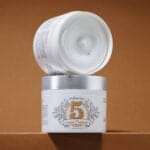 Cremă de corp albă, densă, în borcan alb cu capac argintiu, etichetă auriu și detalii despre uleiurile nutritive.