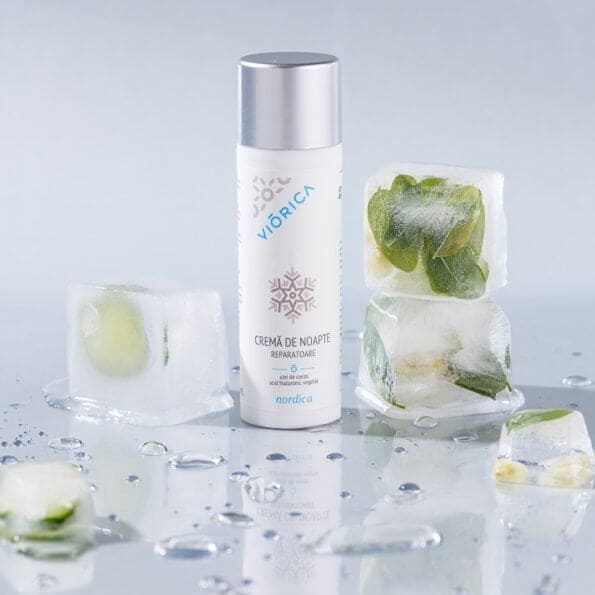 Cremă de noapte reparatoare Nordica, ambalaj alb, capac argintiu, înconjurat de cuburi de gheață cu plante.