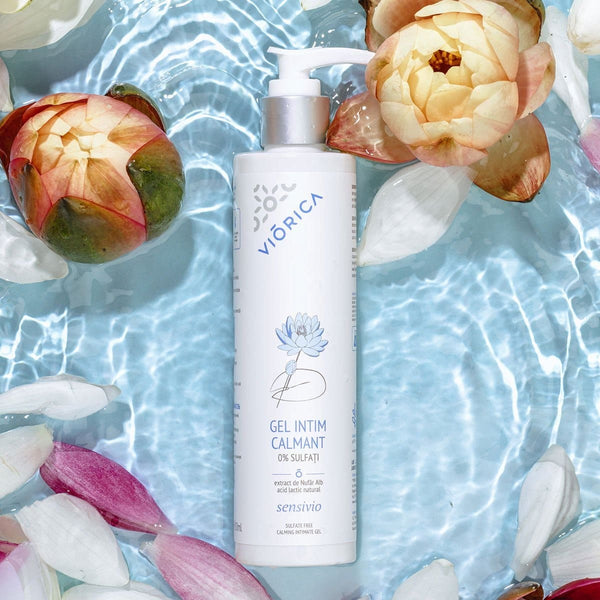 Gel Intim Calmant Viorica Sensivio 0% sulfați, recipient alb, capac dispenser, pe fundal floral acvatic.