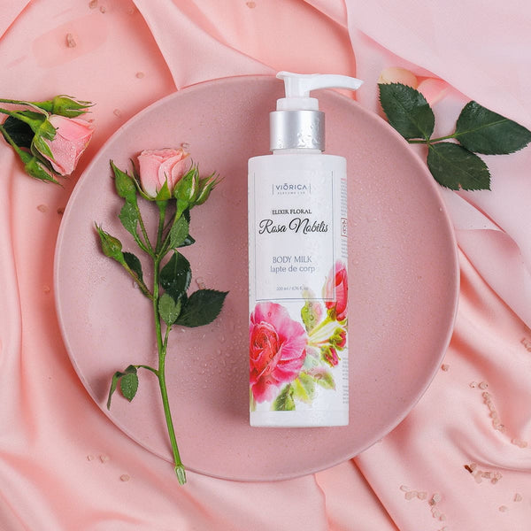 Lapte de corp Rosa Nobilis, 200 ml, într-un flacon alb cu pompiță, decorat cu trandafiri roz pe fundal roz.