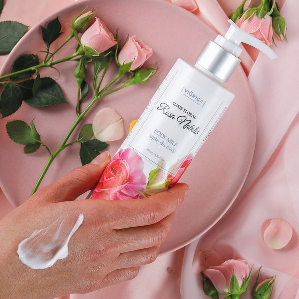 Detaliu lapte de corp Rosa Nobilis cu extract floral, pe fundal roz cu trandafiri.