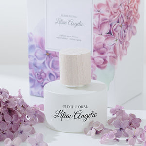 Sticlă parfumată „Elixir Floral Liliac Angelic” cu capac din piele, flori liliachie în fundal.