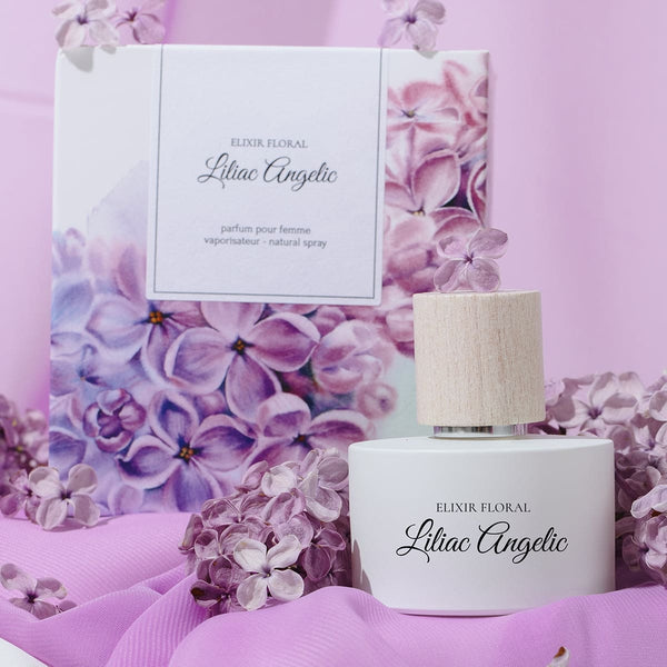 Parfum „Elixir Floral Liliac Angelic” în sticlă albă cu capac texturat, carton cu flori liliac pe fundal roz.