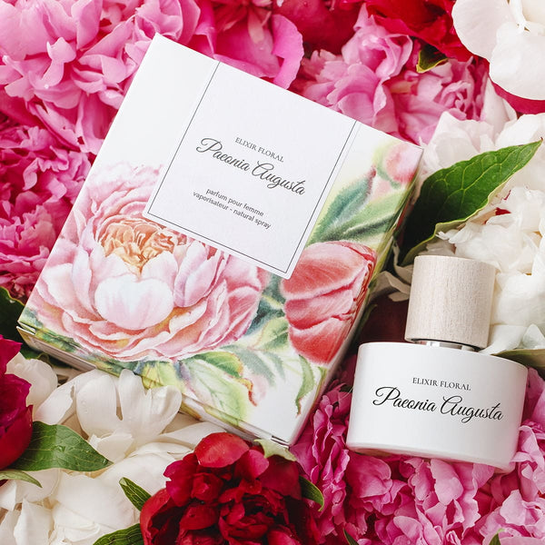 Parfum femei „Elixir Floral Paeonia Augusta”, ambalaj floral, capac lemn, sticlă albă, pe fundal trandafiri roz și alb.