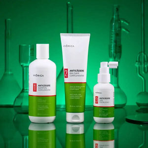 Set șampon anticădere Viorica cu balsam și ser, ambalaje albe și verzi, fundal sticlă verde.