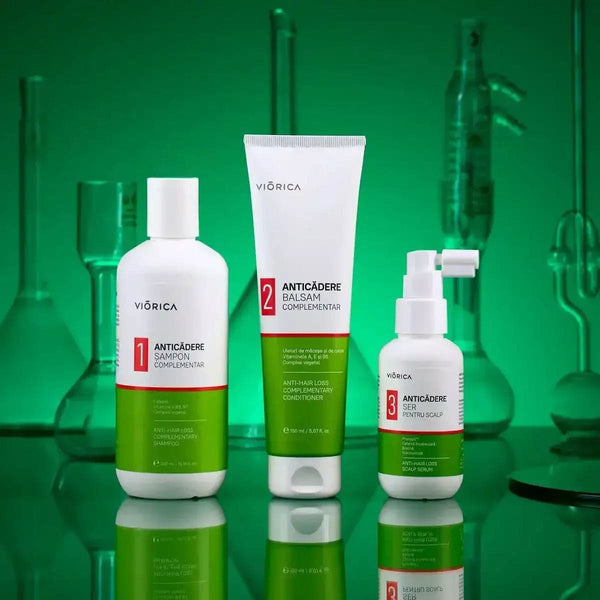 Set șampon anticădere Viorica cu balsam și ser, ambalaje albe și verzi, fundal sticlă verde.
