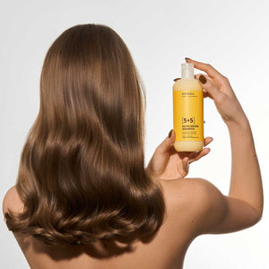 Flacon galben de șampon Viorica 5+5 pentru păr degradat, ținut de mâna unei femei cu păr neted și sănătos.