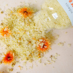 Sare de baie cu mușețel și gălbenele, textură granulată, nuanțe galben-portocalii.