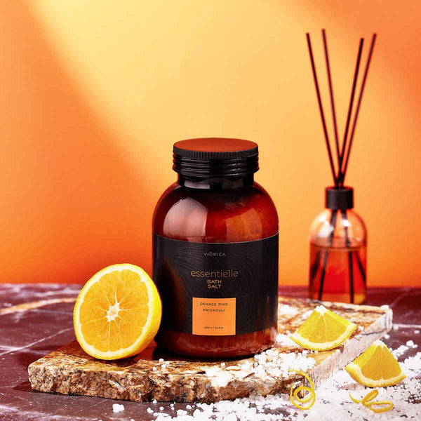 Sare de baie Viorica Essentielle cu extract de portocală și patchouli, într-un recipient ambra, pe fundal portocaliu.
