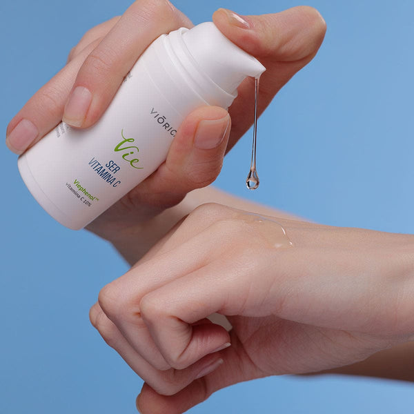 Ser Viorica Vie cu 10% Vitamina C, flacon alb, textură lichidă, aplicat pe piele, fundal albastru.