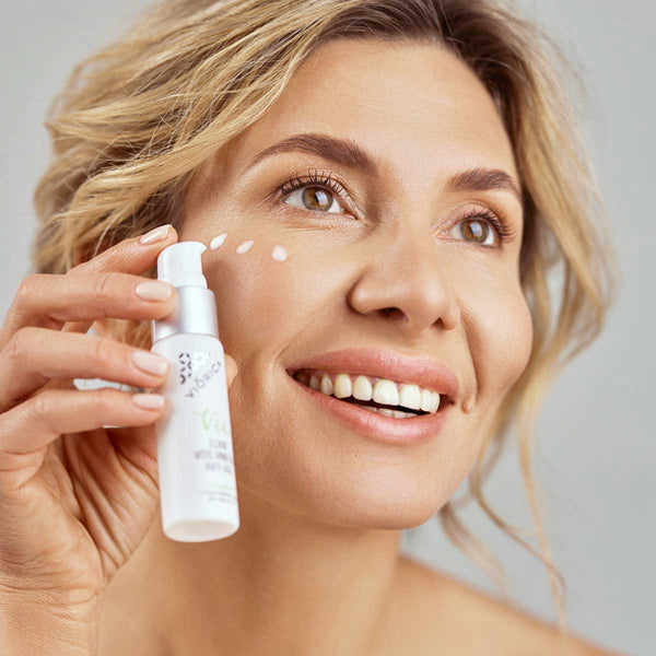 Femeie aplicând ser Vitis Vinifera Anti-Age Viorica Vie din ambalaj alb cu pompiță.