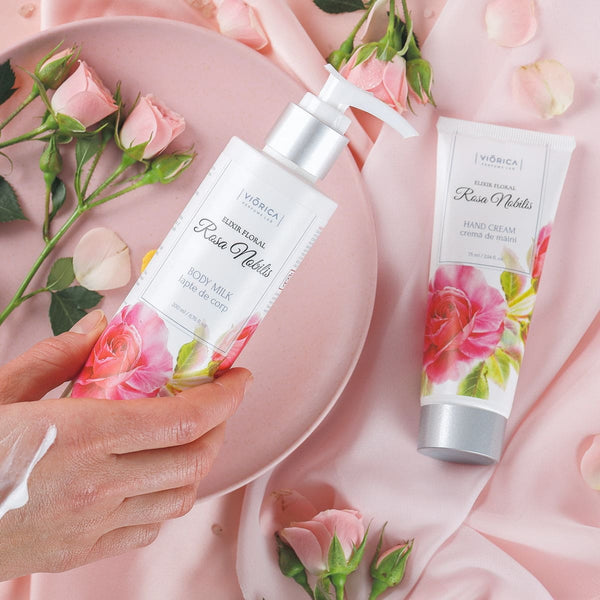 Set pentru corp cu flori roz, crema de mâini și lapte de corp, design elegant pe fundal de satin.